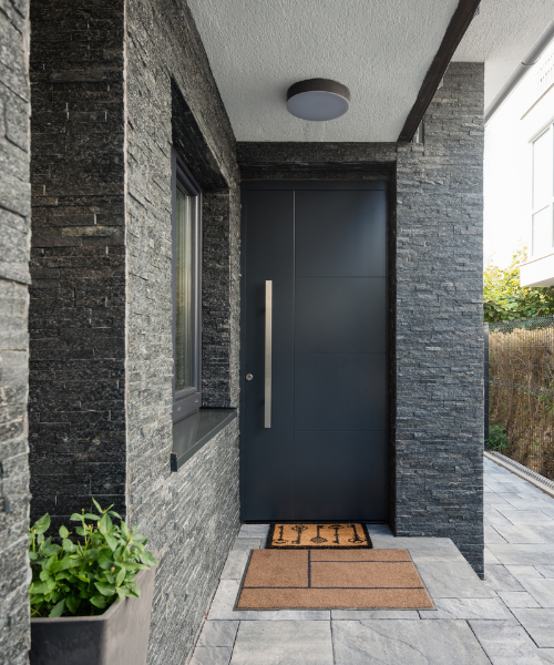 patio floor tiles - image of front entrance to house, black door with dark stacked stone walls and grey stone floor tiles, entry matt and pot plant